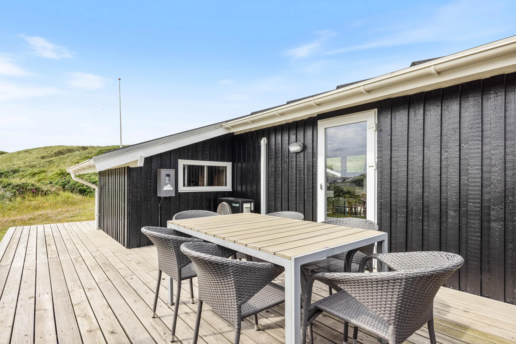 Una terraza de madera con asientos y una mesa junto a una pared exterior oscura.