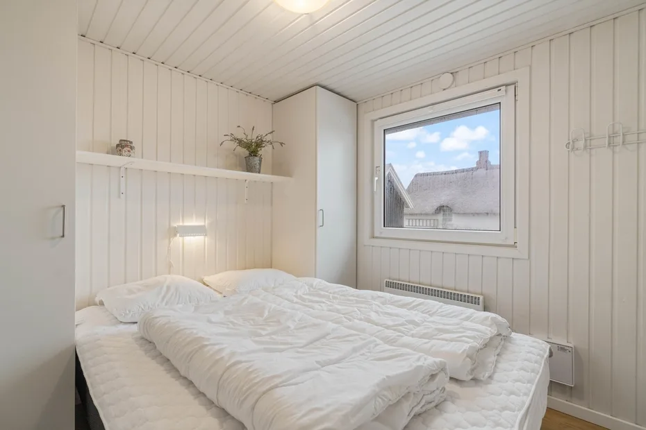 Un dormitorio con una cama bajo una ventana con vistas a tejados cercanos.