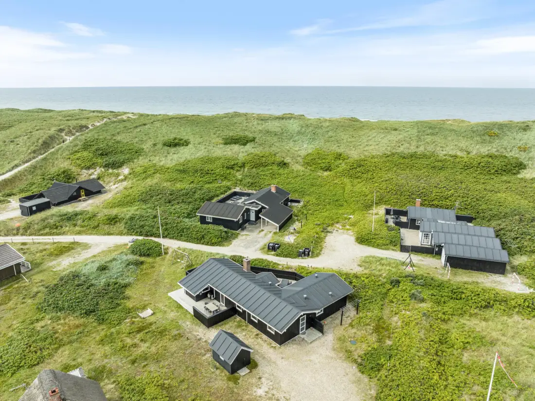 Vista aérea de varias casas entre dunas cubiertas de hierba junto al mar.