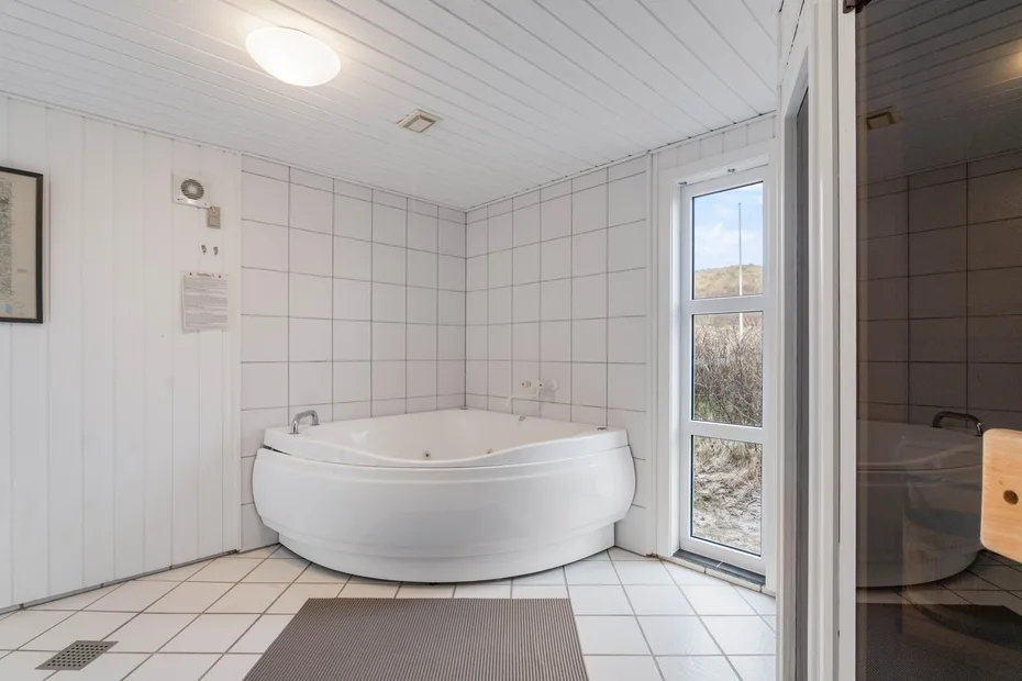 Un baño con azulejos, una bañera grande y una ventana alta.