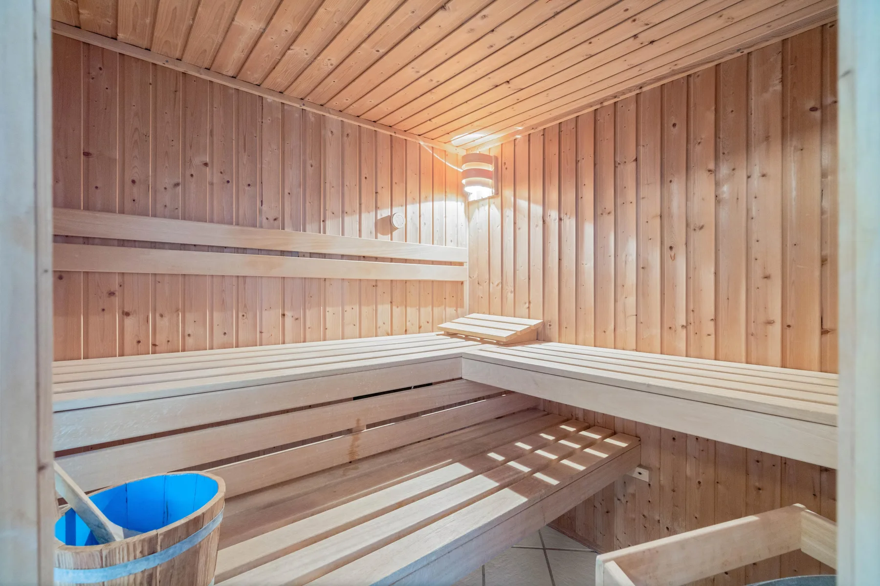 Una sauna de madera con bancos en varios niveles y un pequeño cubo azul.