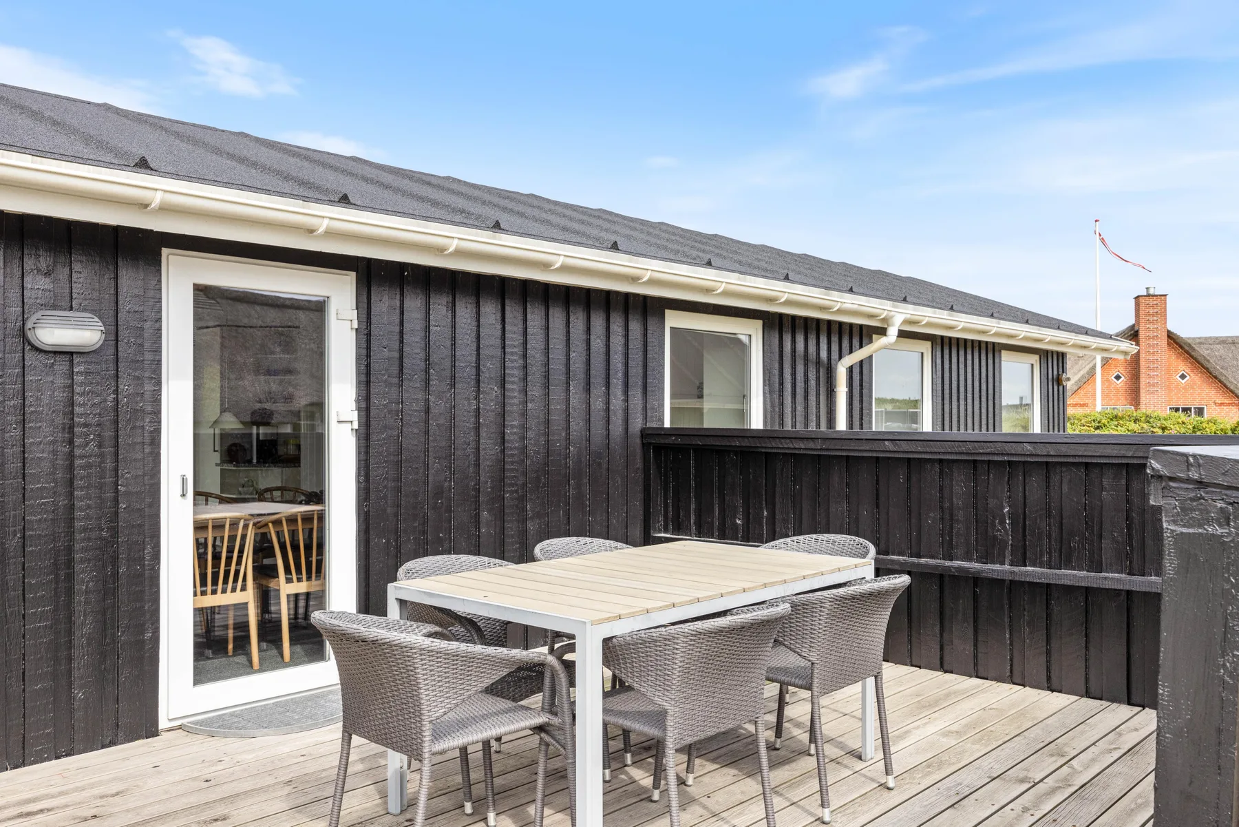 Una terraza de madera con mesa y sillas de exterior junto a una casa oscura.