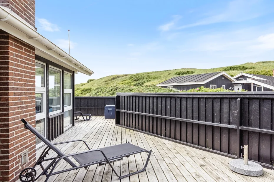 Una terraza exterior de madera con asientos reclinables da a casas vecinas y colinas verdes.