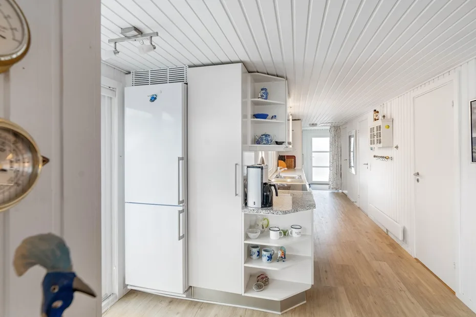 Una cocina luminosa con refrigerador, estantes abiertos y un largo piso de madera.