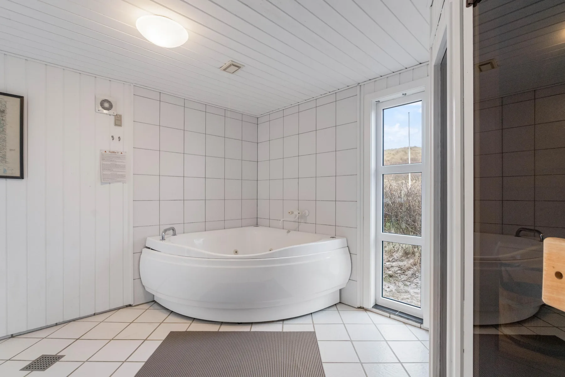 Un baño alicatado con una bañera de esquina junto a una ventana alta.