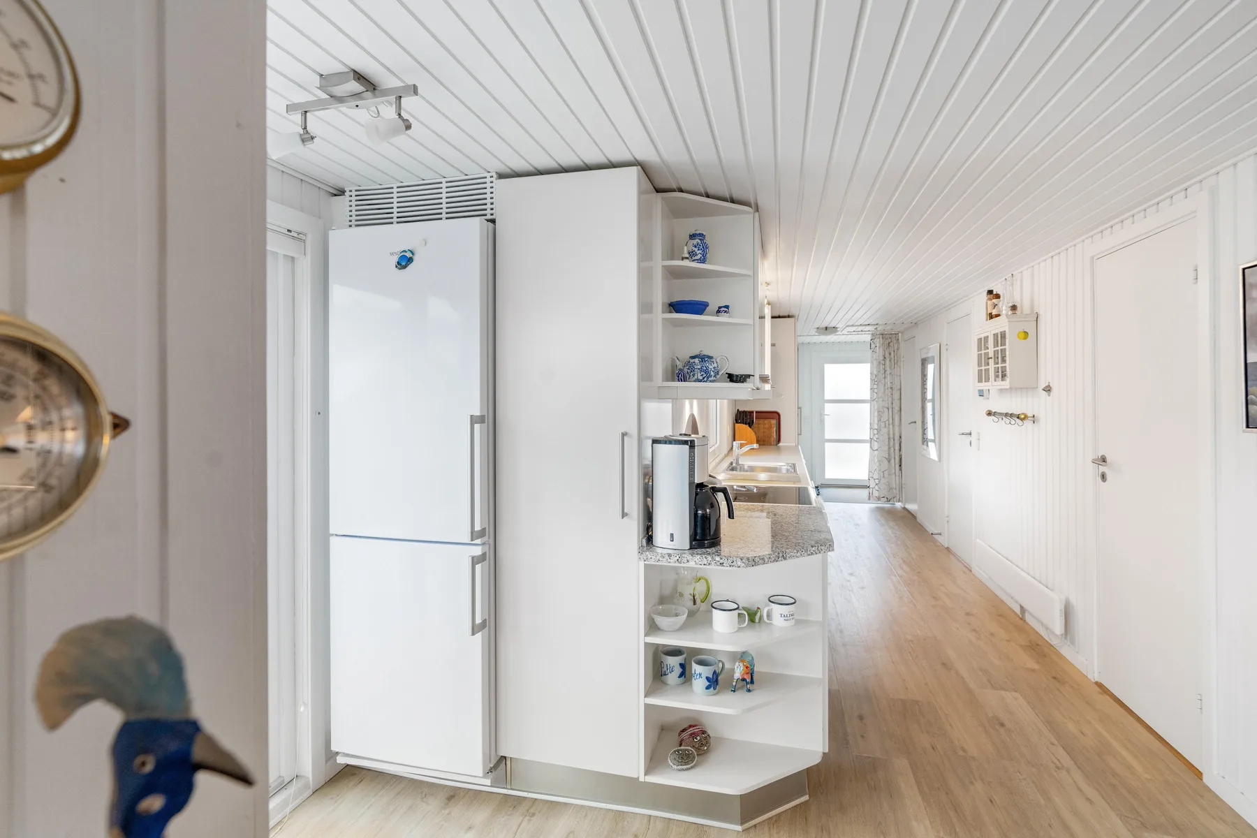 Una cocina luminosa con refrigerador, estantes abiertos y una encimera larga.