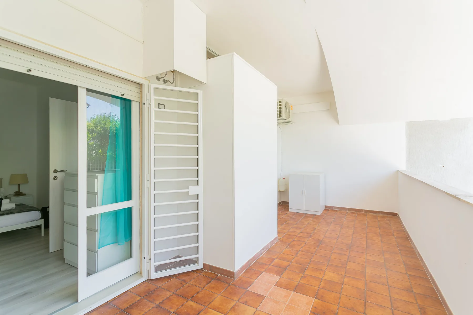 A tiled terrace beside a sliding glass door and a white louvered panel.