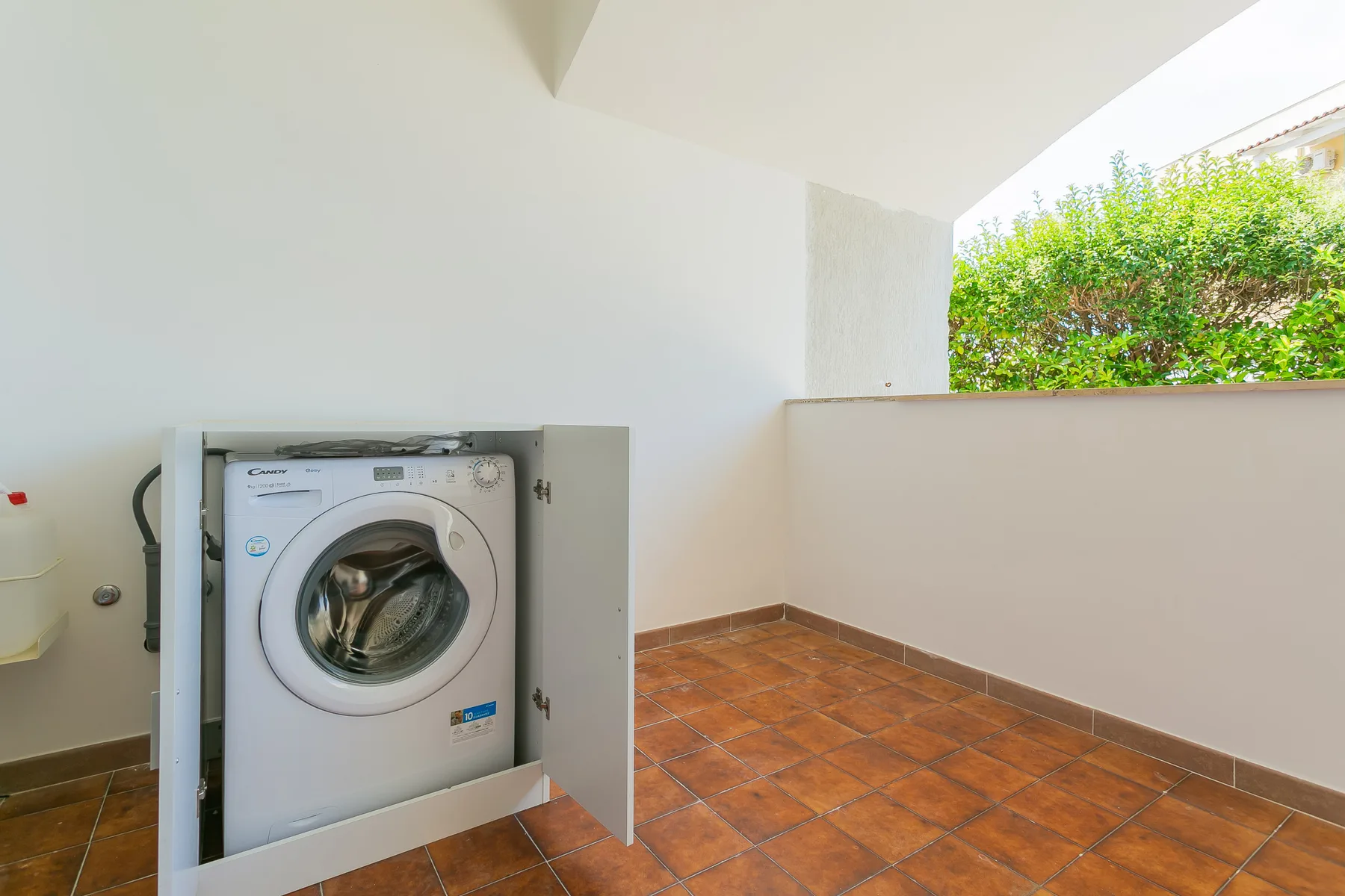 A covered utility area with a washing machine and tiled floor.