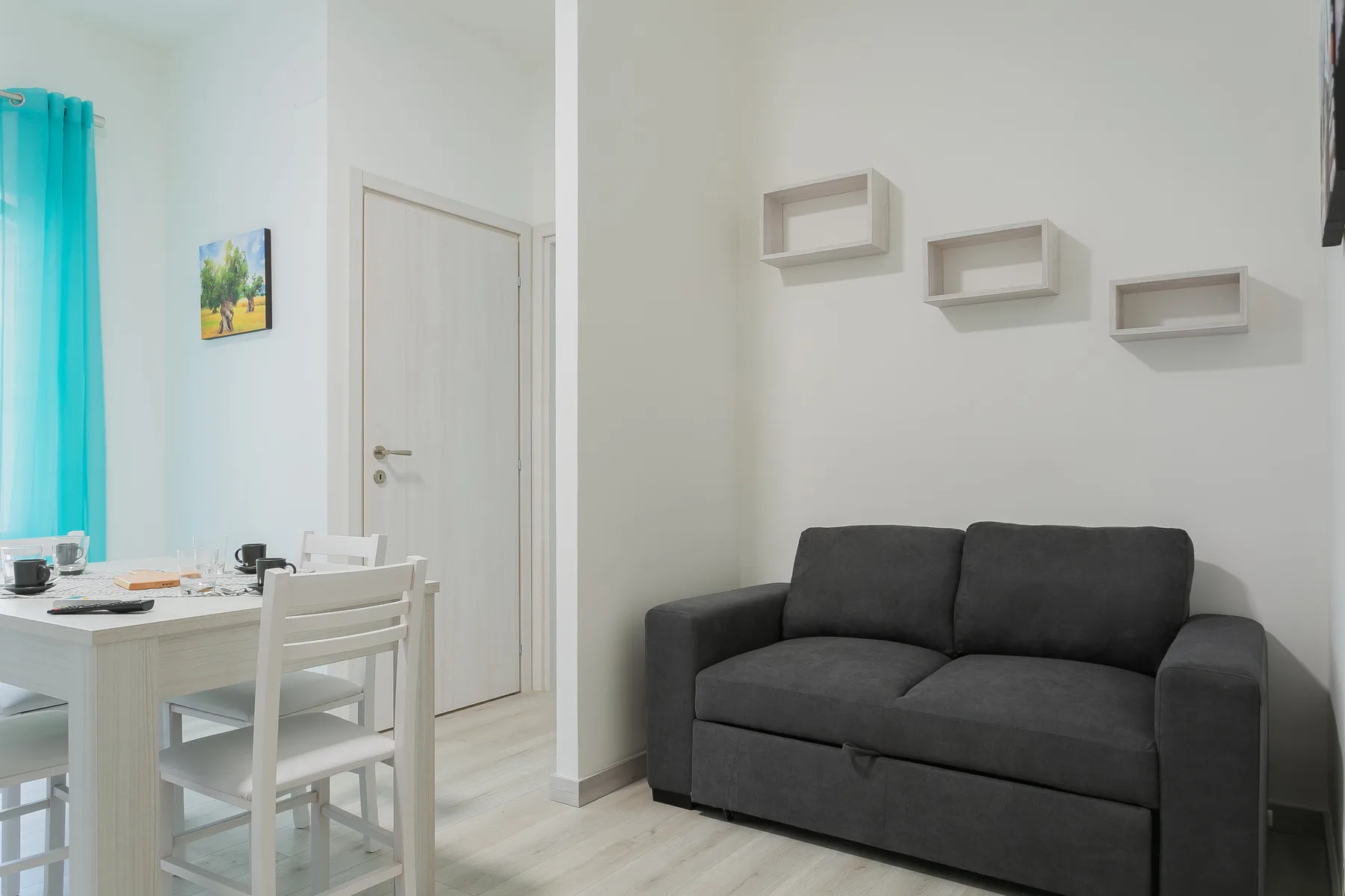 A bright living and dining area with a dark sofa and white dining table.