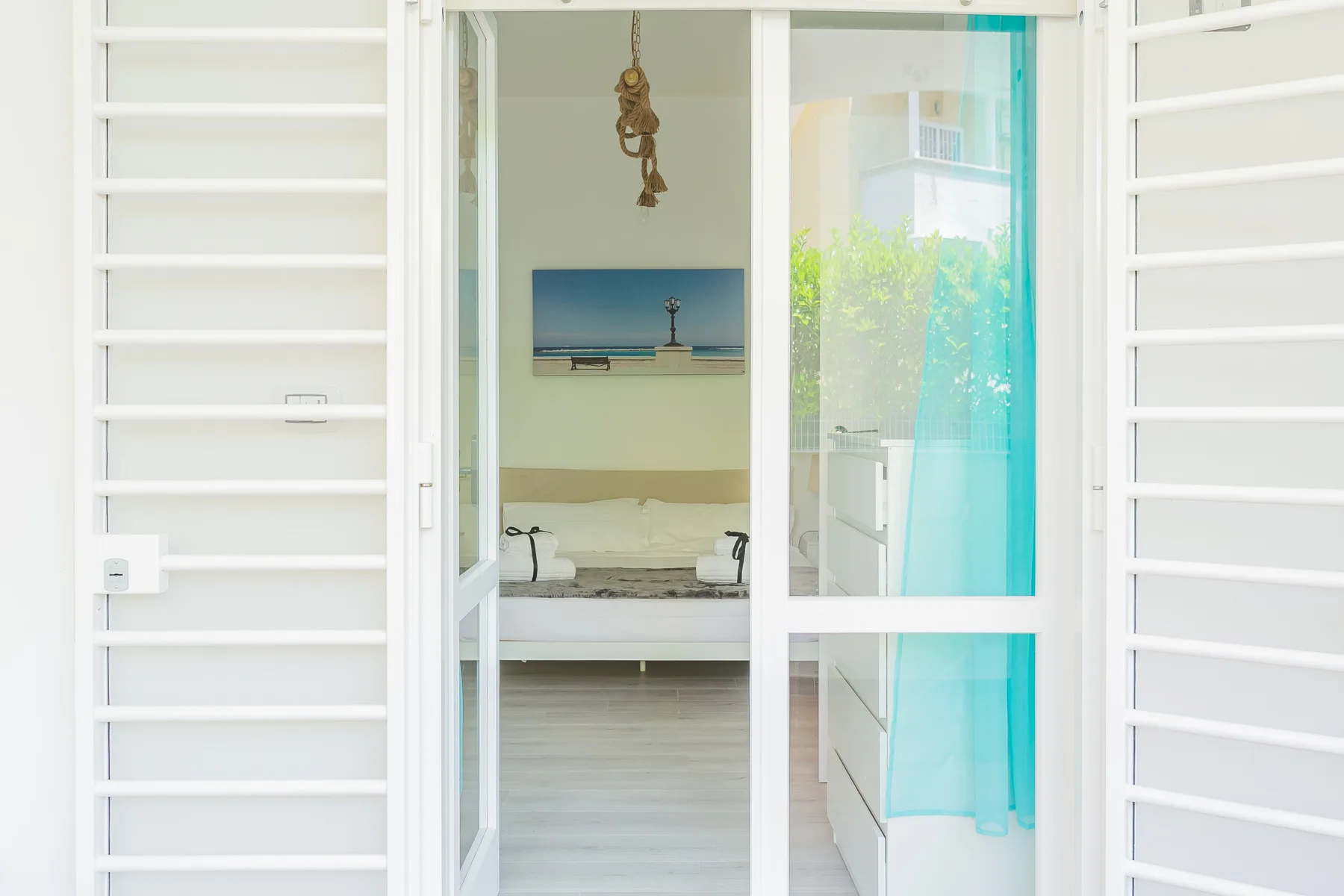 A bright bedroom is visible through an open doorway, with a bed beneath a seaside picture.