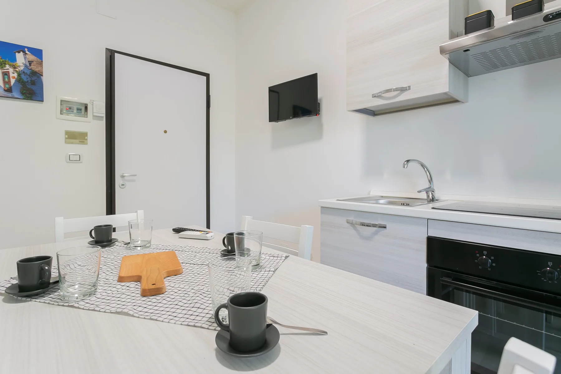 A dining area beside a compact kitchen, with a set table and wall-mounted television.
