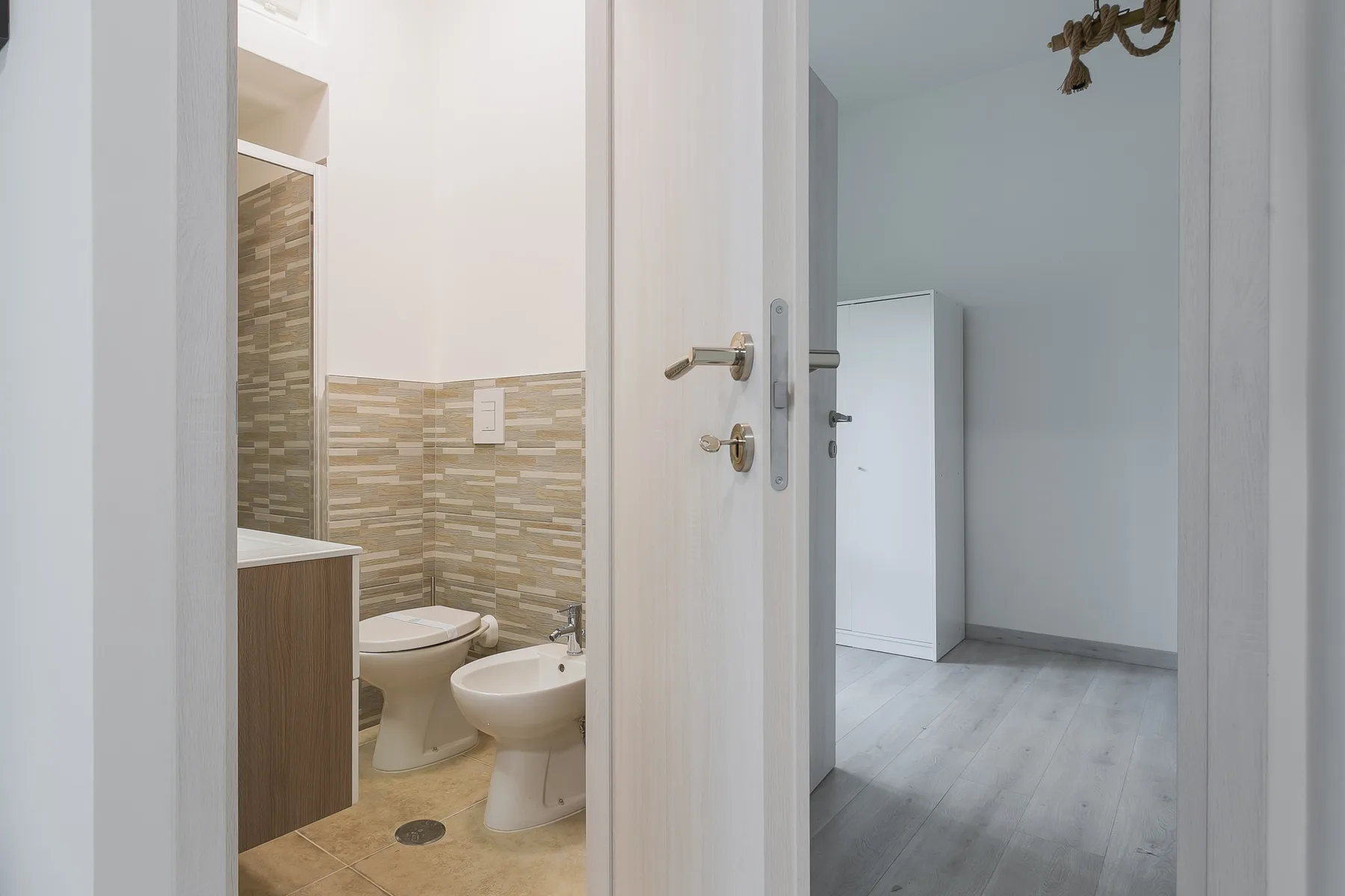 An open doorway reveals a bathroom with a toilet and sink beside a light-floored room.