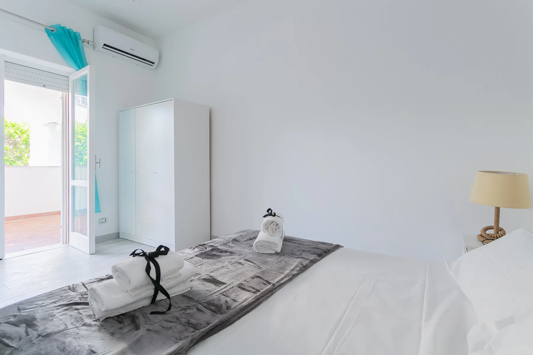 A bright bedroom with a neatly made bed and an open balcony door.
