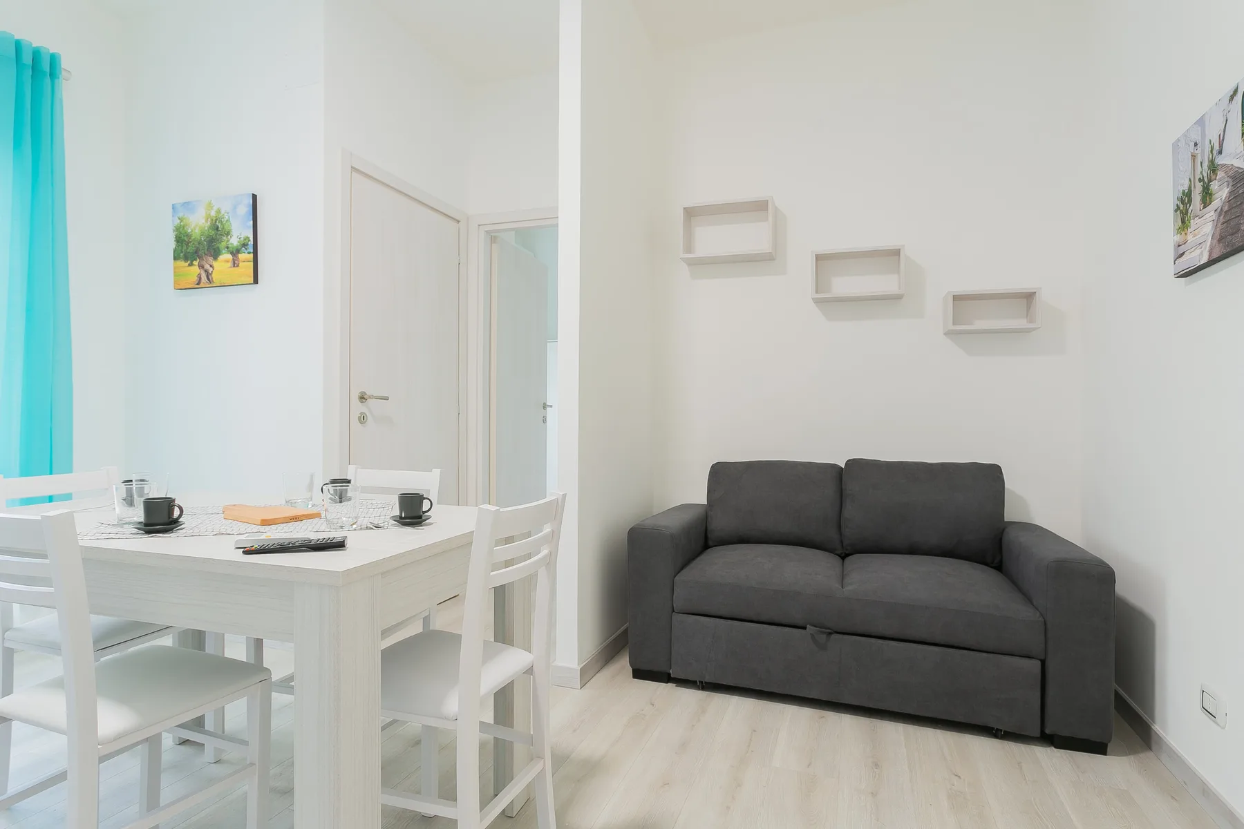 A bright dining area with a white table and chairs beside a gray sofa.