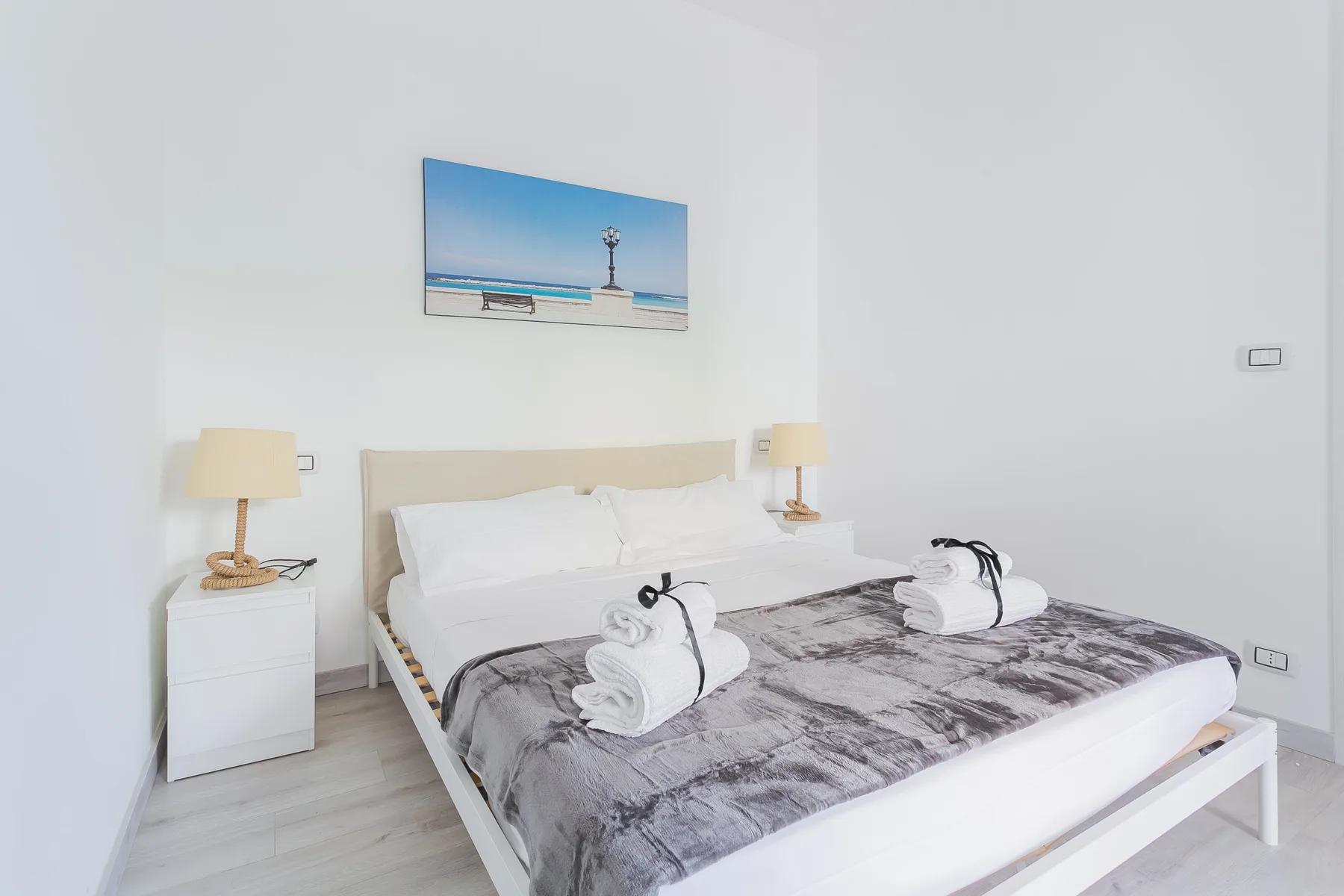 A bright bedroom with a neatly made bed and a beach picture above it.