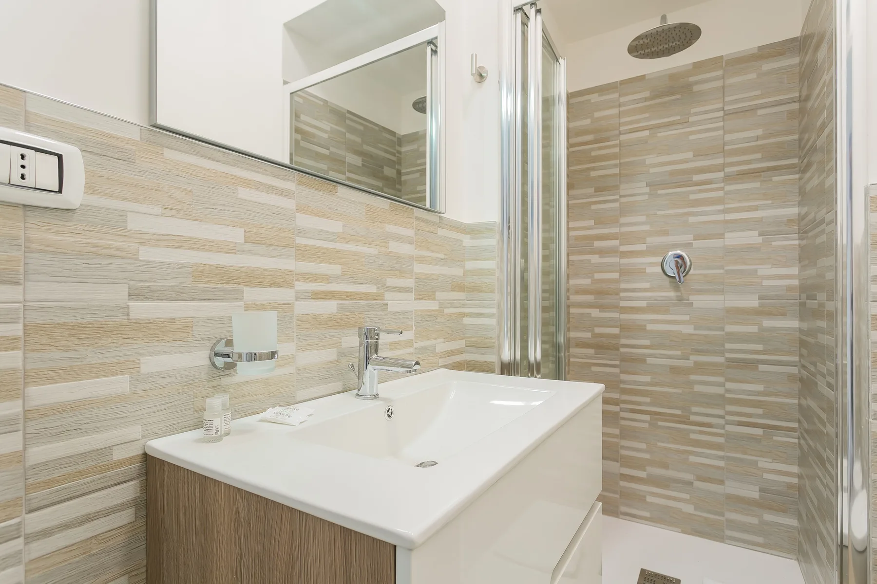 A bathroom with a white sink, wall mirror, and tiled shower area.