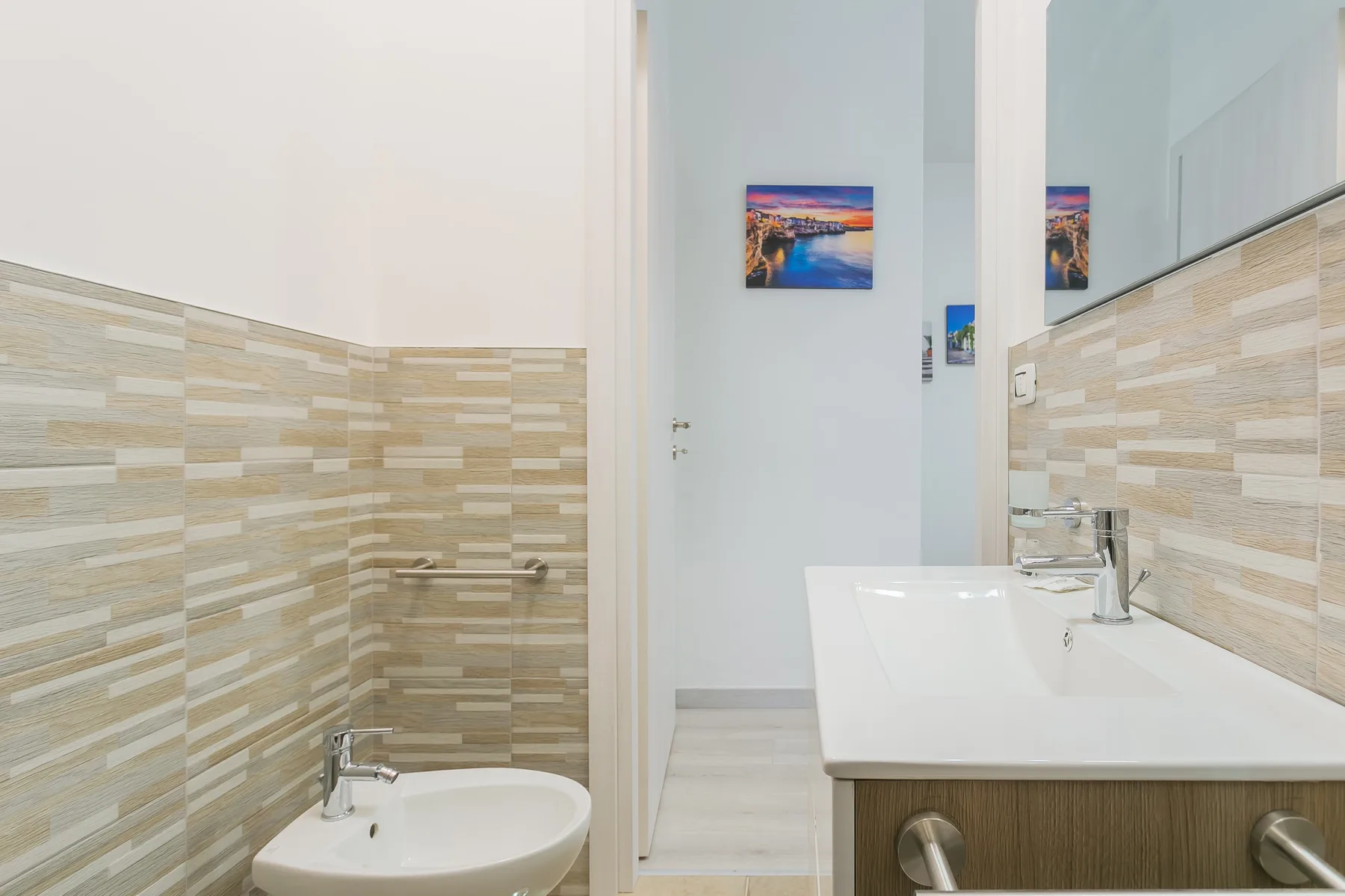 A bathroom with a sink, bidet, and beige patterned wall tiles.