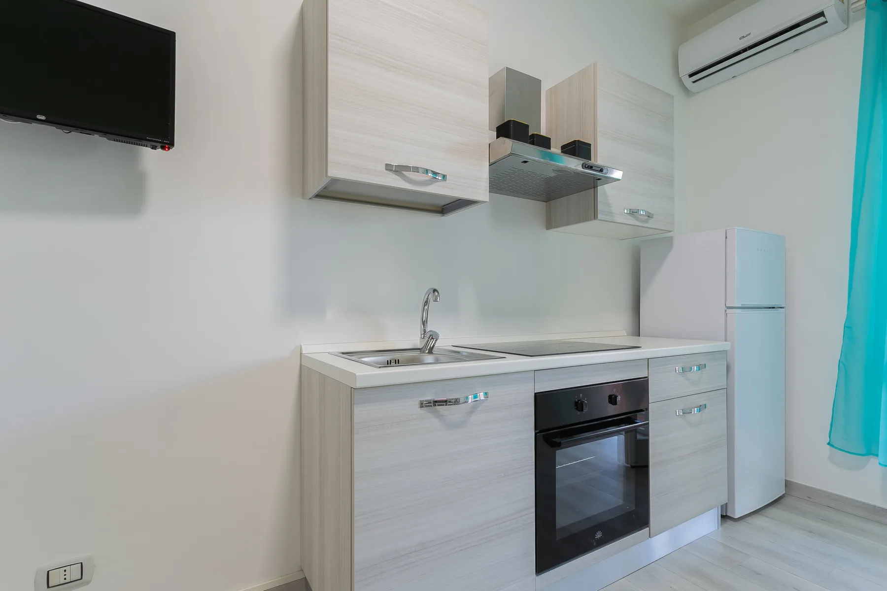 A compact kitchen with light cabinets, a refrigerator, and an oven.