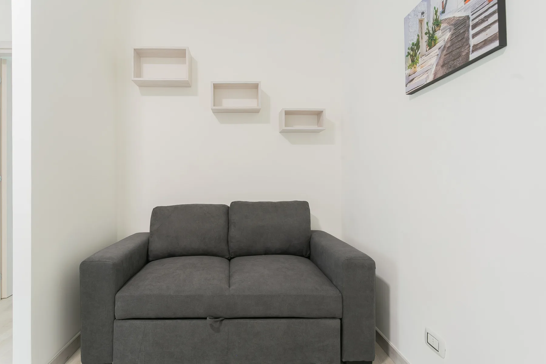 A living room with a gray sofa and small wall shelves.