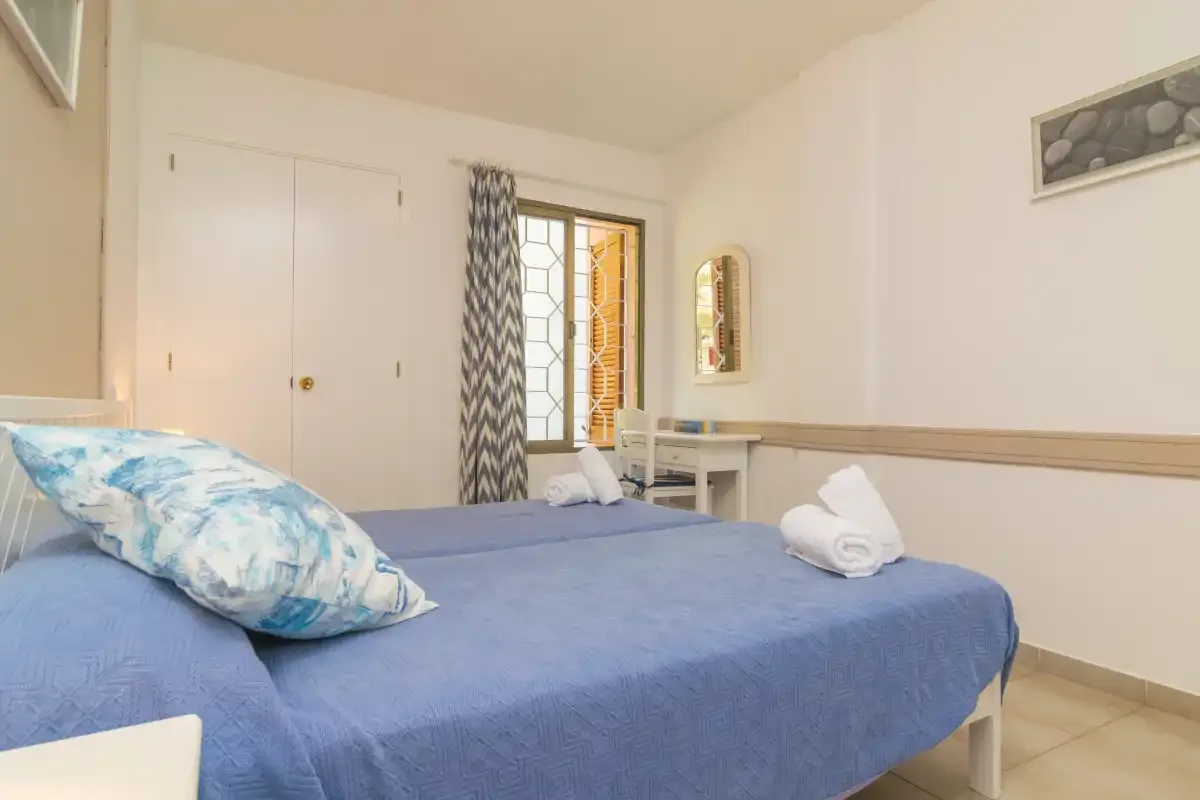 A bedroom with a blue bed and a small table beside the window.