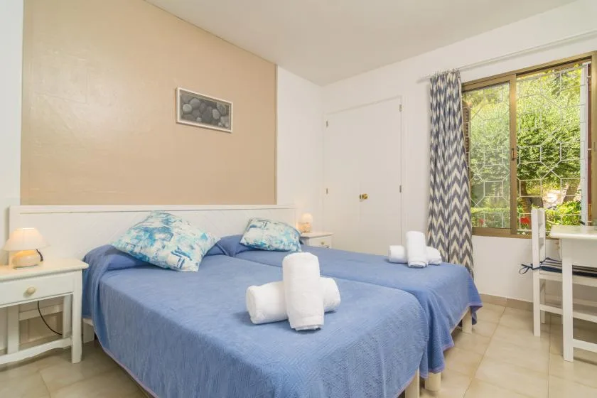 A bedroom with blue-covered beds and a window overlooking leafy trees.