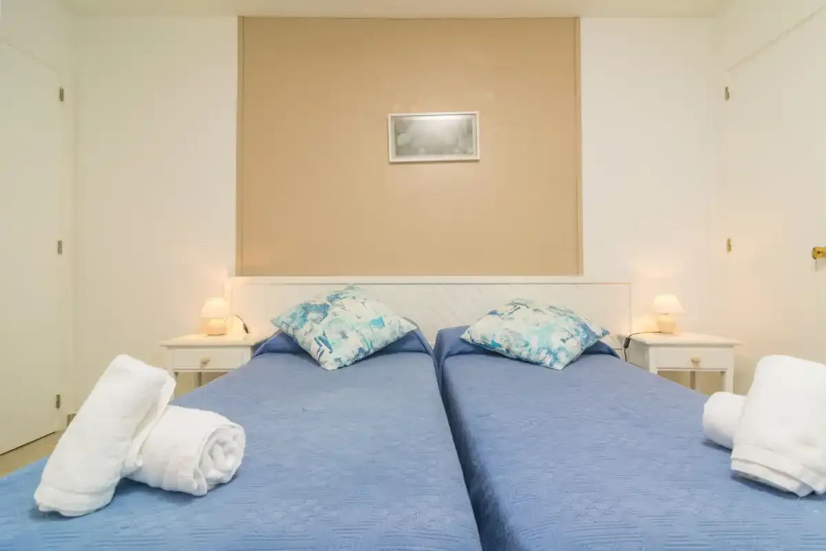 A bedroom with two blue beds and matching bedside tables.