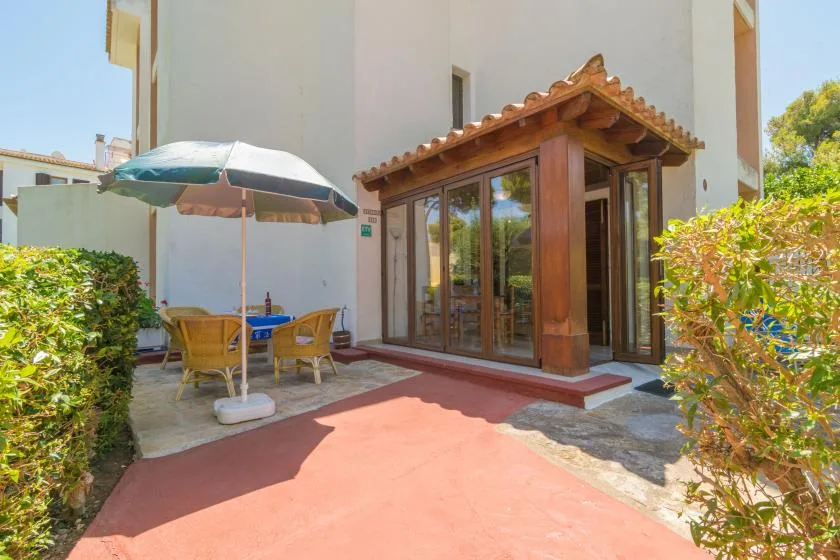 An outdoor patio with a shaded table beside a glass-door entrance.