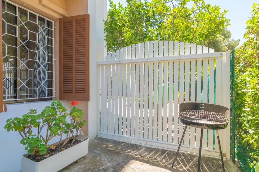 A small patio with a white gate, potted plants, and a grill.