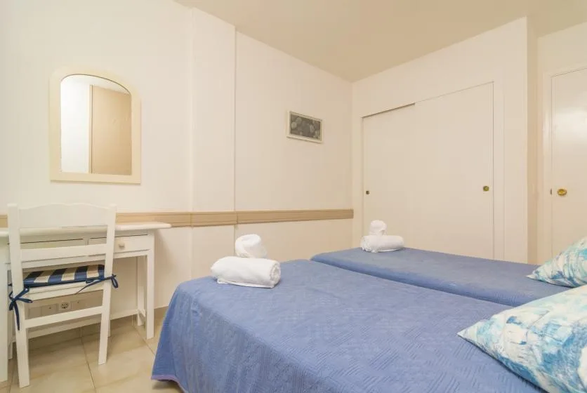 A bedroom with two beds covered in blue bedding and a small desk.