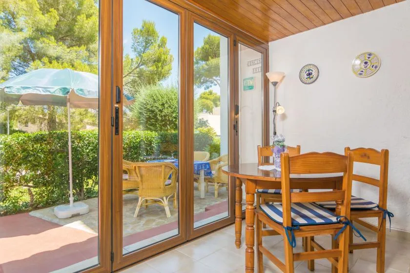 A dining area with wooden seating sits beside large glass doors opening onto greenery.