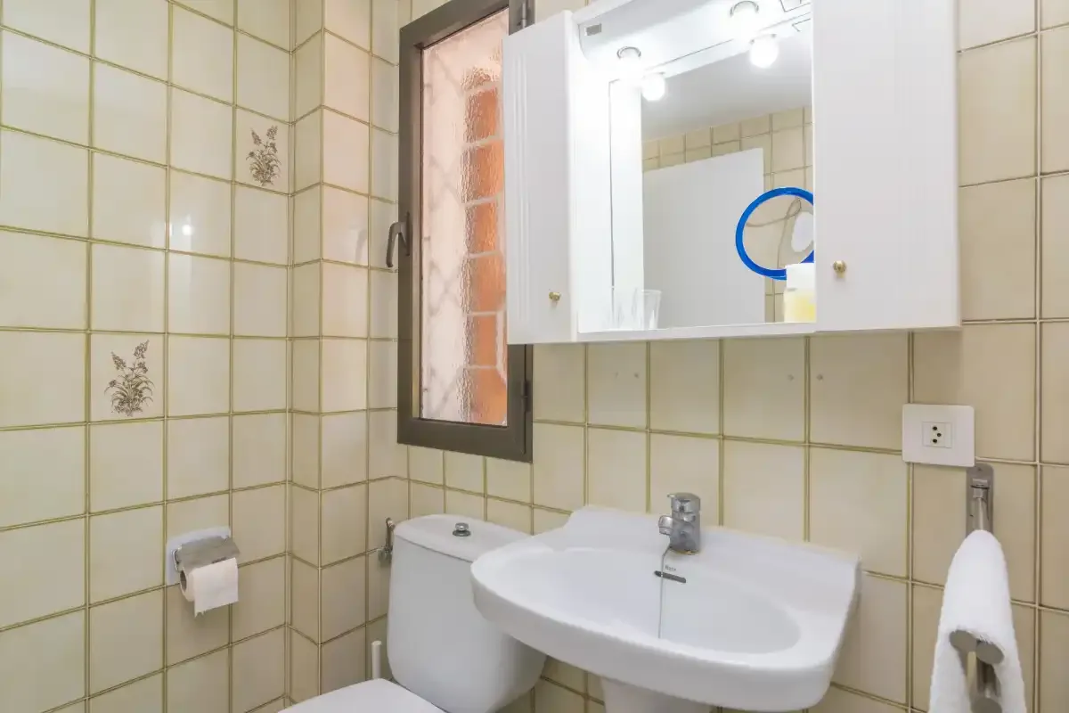 A tiled bathroom with a sink, toilet, and illuminated mirror.