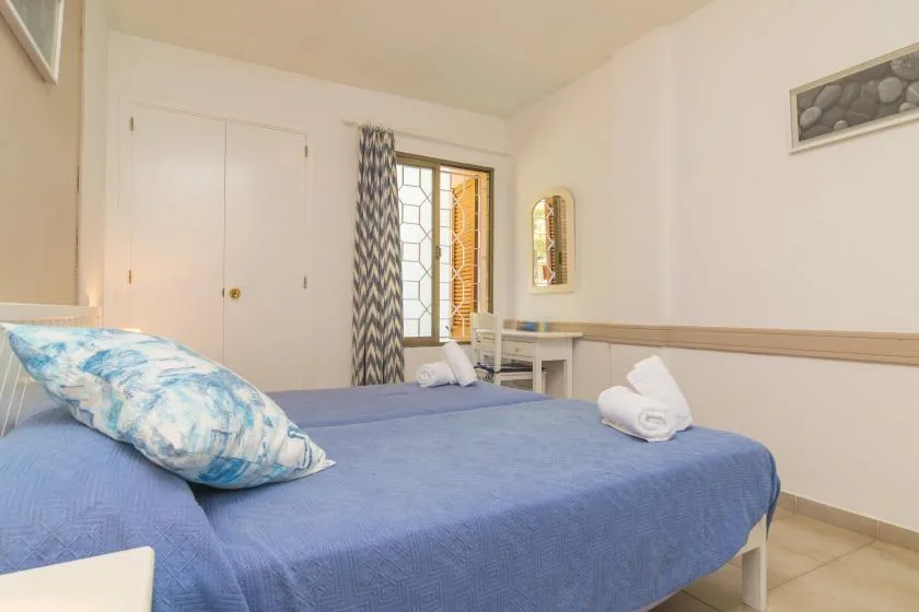 A bedroom with a blue-covered bed and a curtained window.