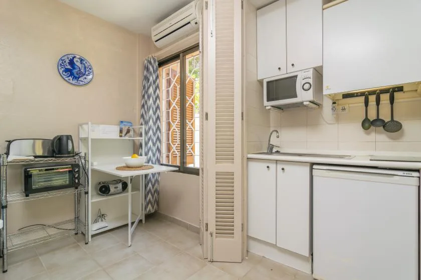 A compact kitchen with white cabinets, a countertop microwave, and a window.