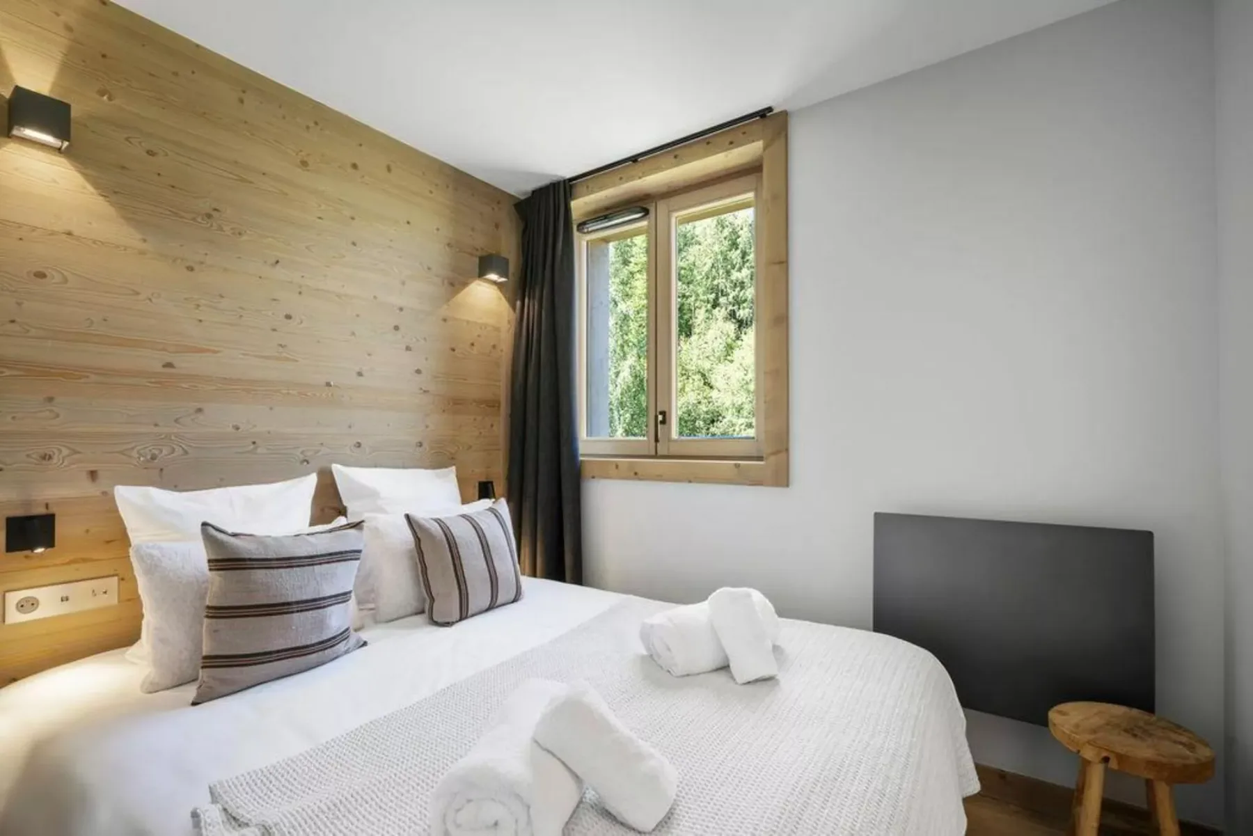 A bedroom with a bed beside a wood-paneled wall and a window.