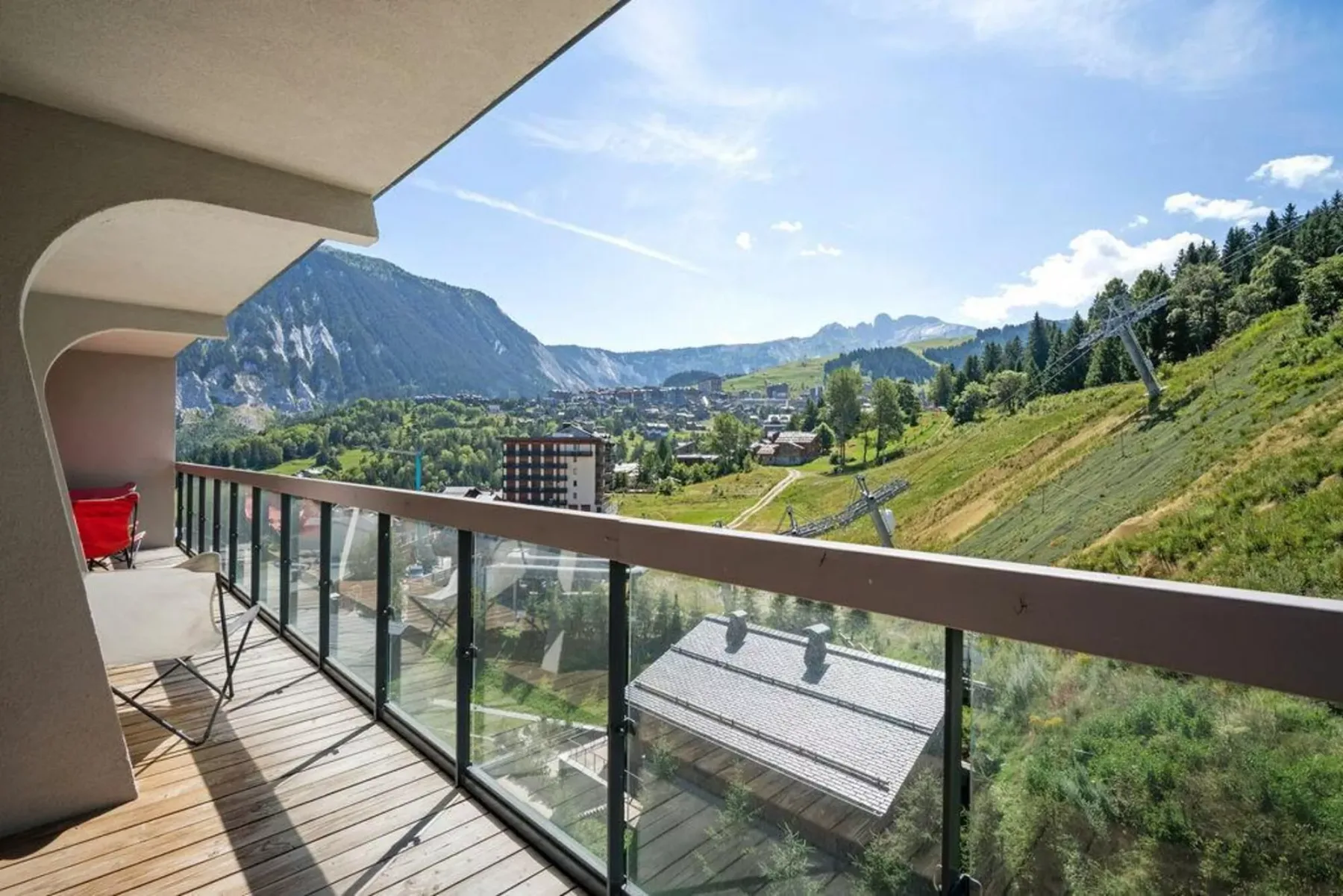 A balcony overlooks a green hillside, forest, and mountain valley.