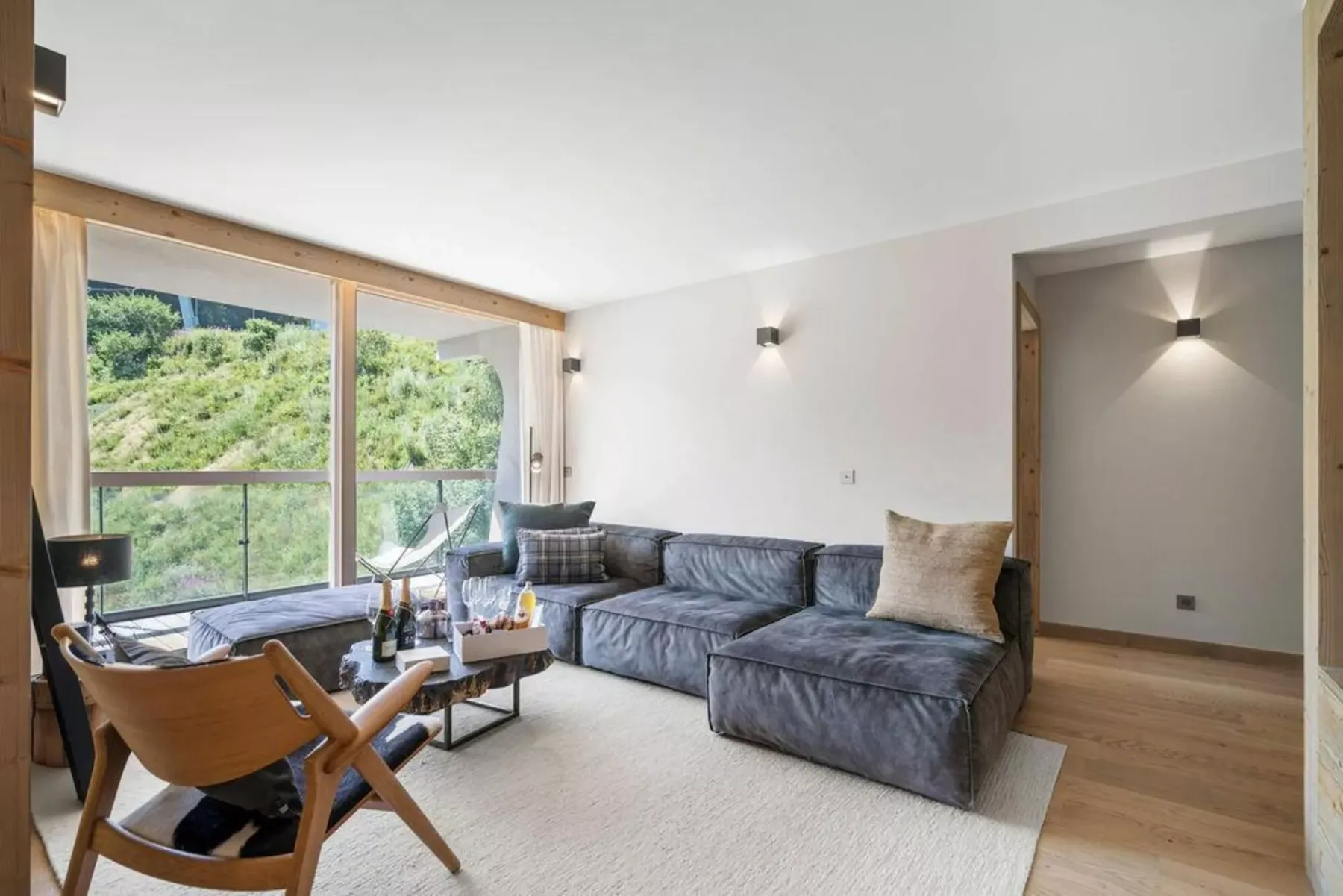 A bright living room with a sectional sofa beside large windows overlooking greenery.