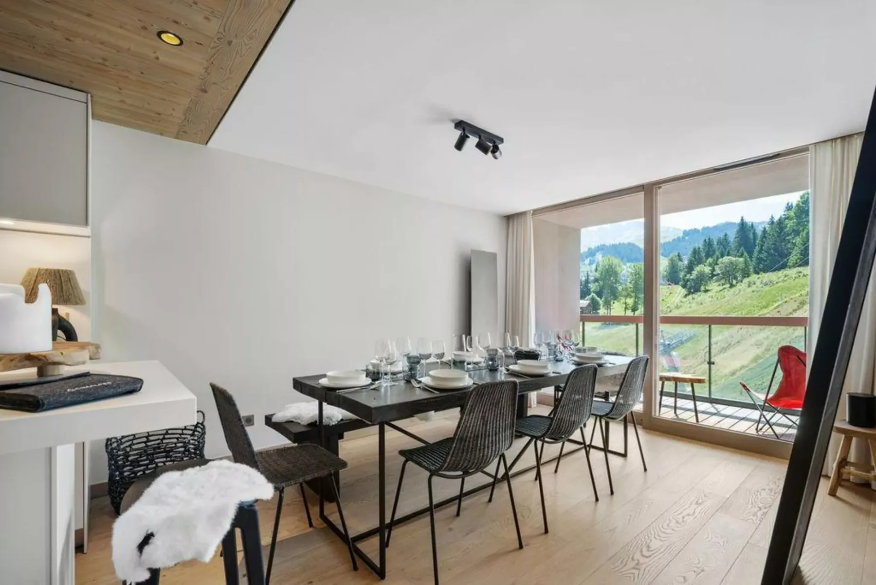 A dining area with a set table beside large windows overlooking a green hillside.