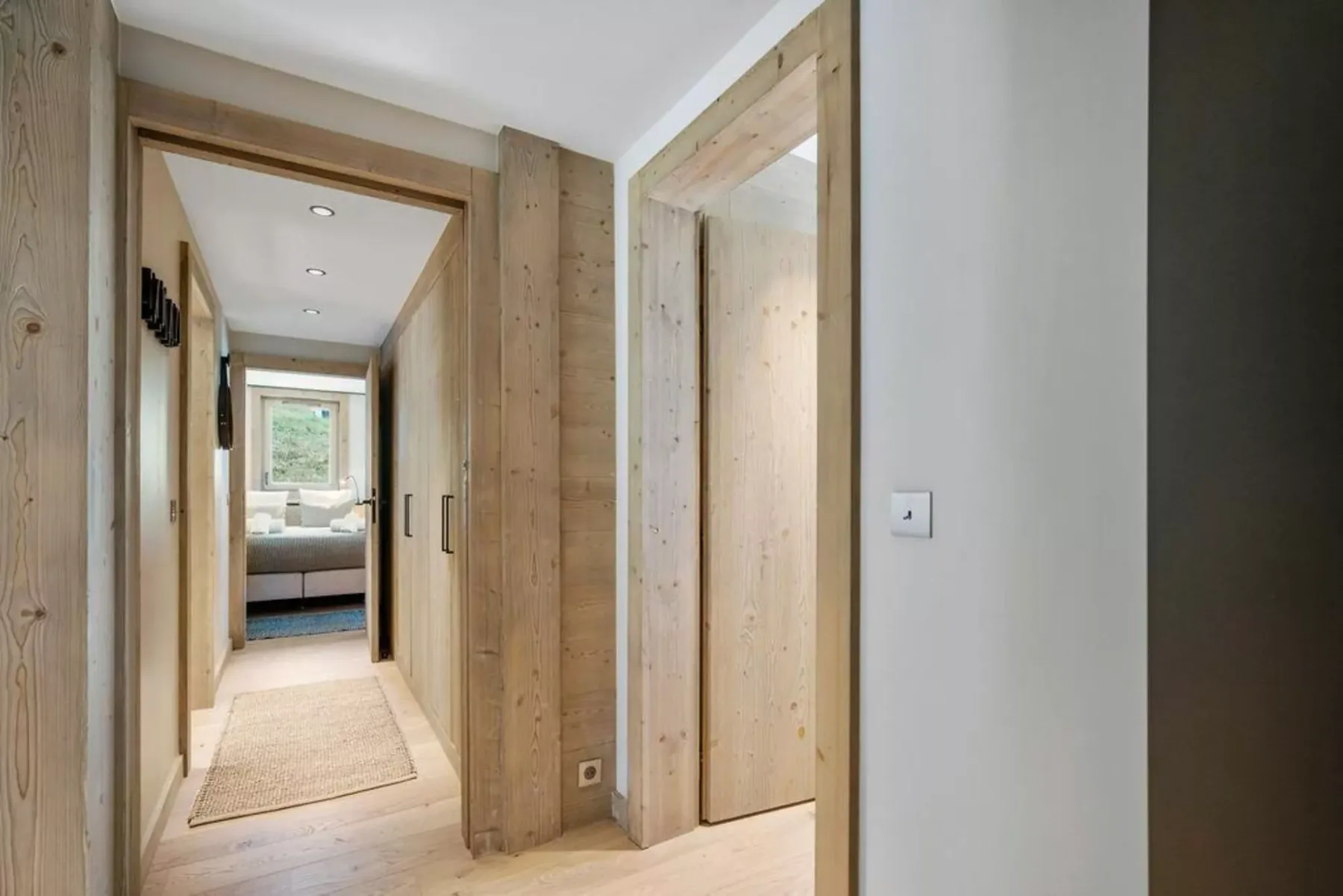 A wood-trimmed hallway leads to a bedroom with a window and bed.