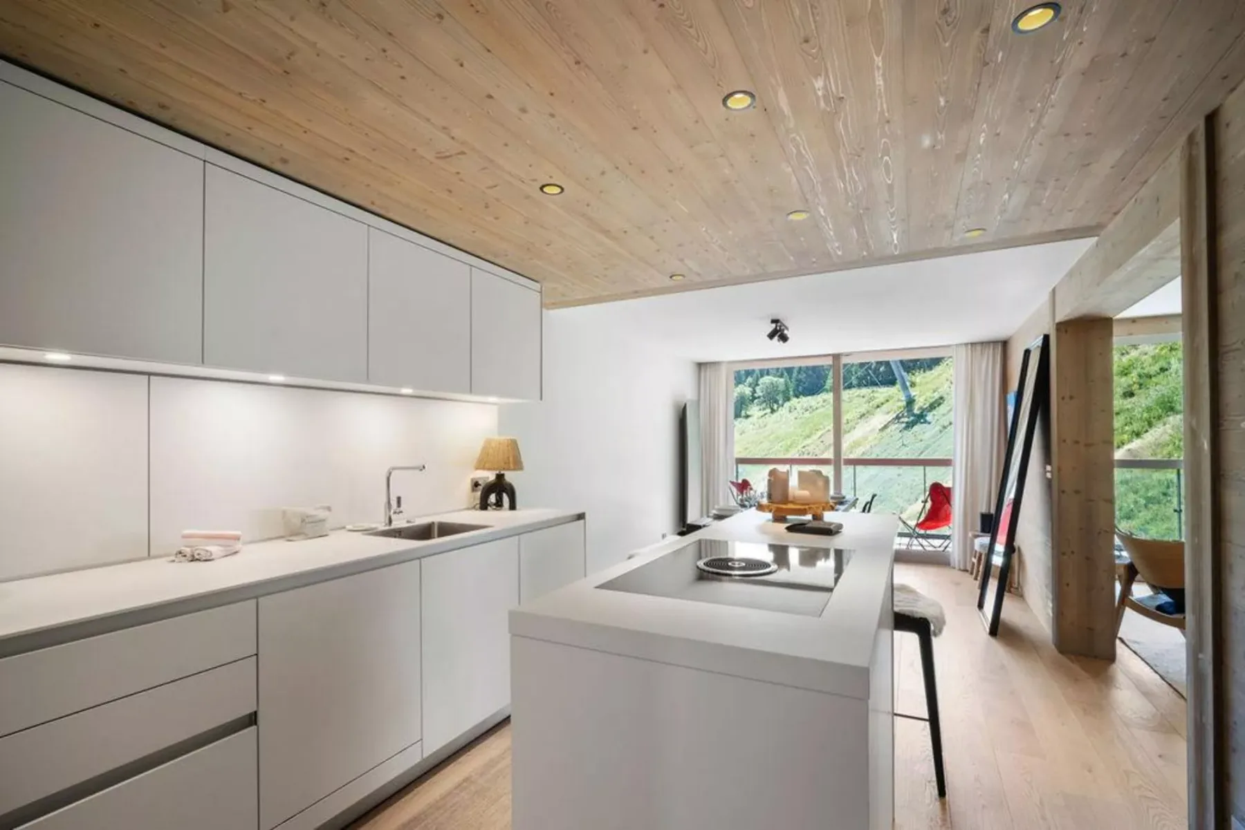 A bright modern kitchen with white cabinetry, a central island, and windows overlooking greenery.