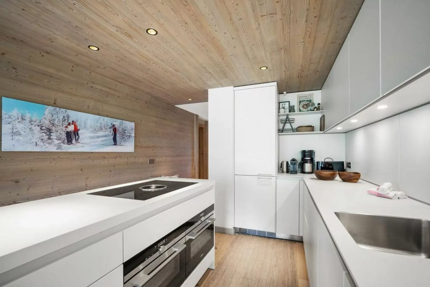 A modern kitchen with white counters, built-in appliances, and wood finishes.