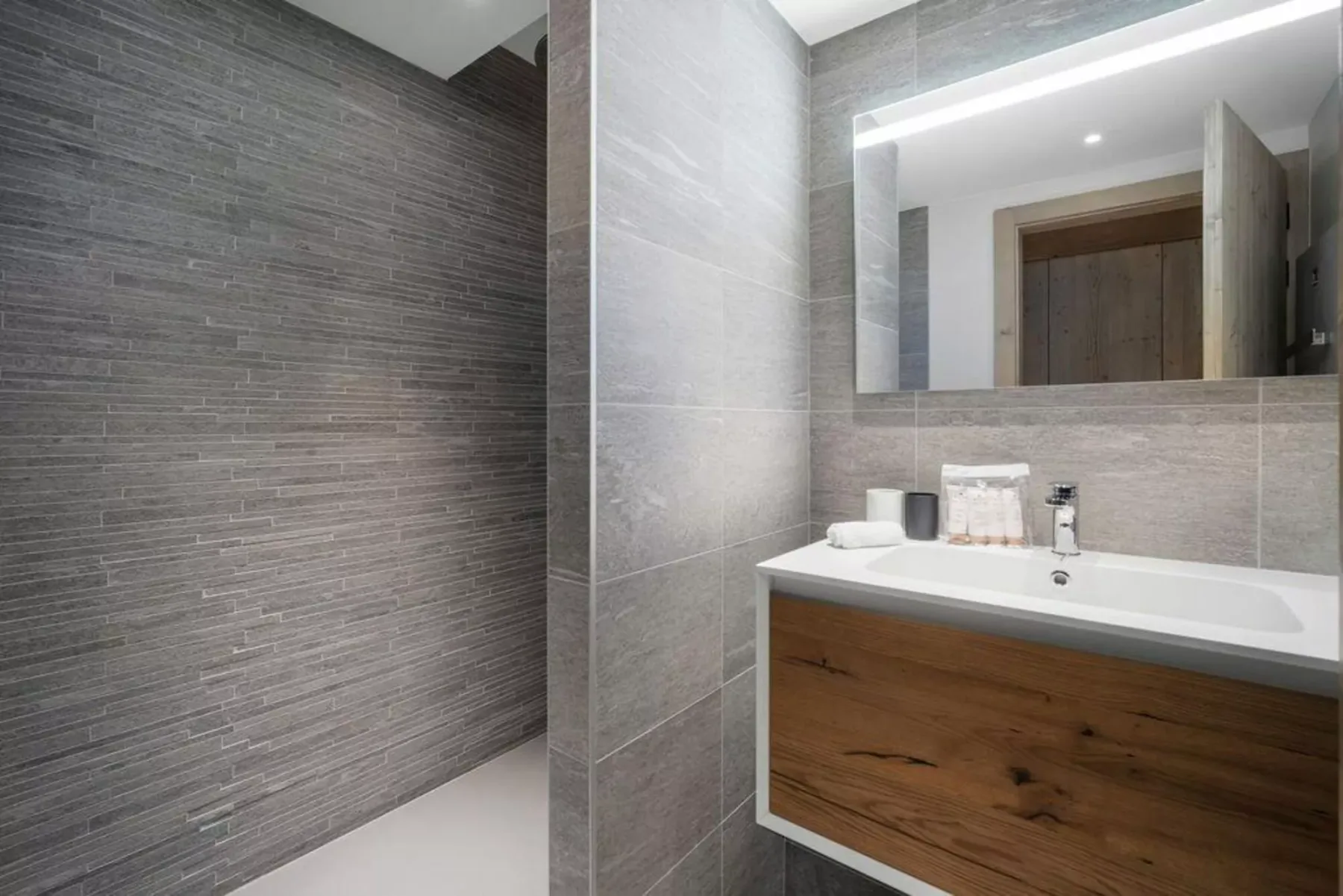 A modern bathroom with a wide mirror above a wood-fronted vanity.