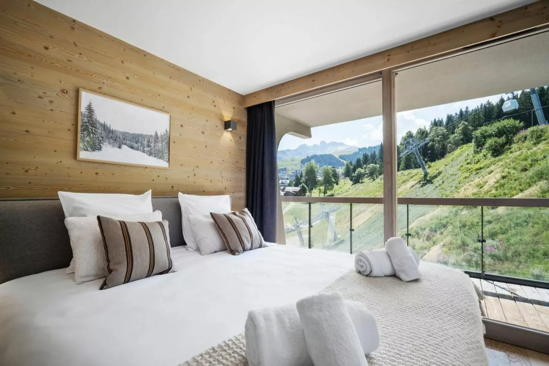 A bedroom with white bedding and large windows overlooking a green mountain landscape.
