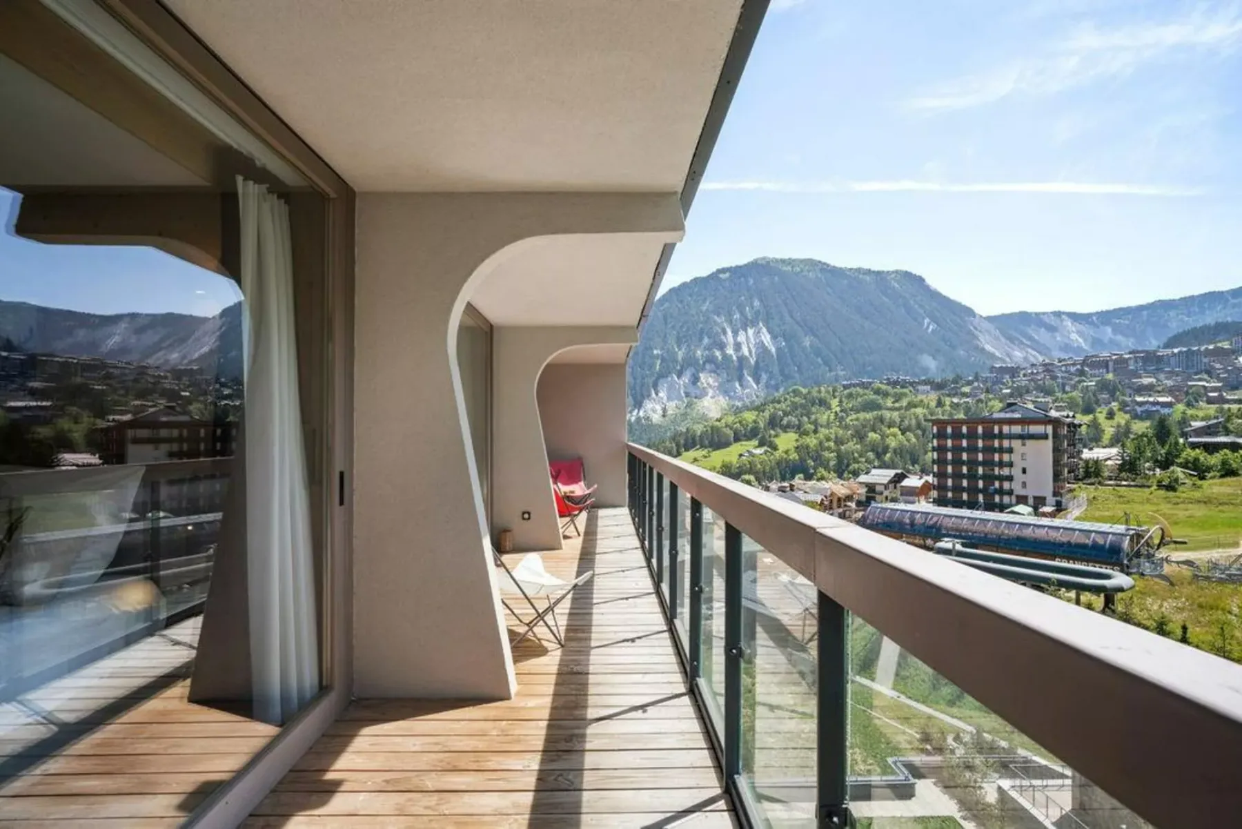 A balcony overlooks a mountain valley, with glass railings along the edge.
