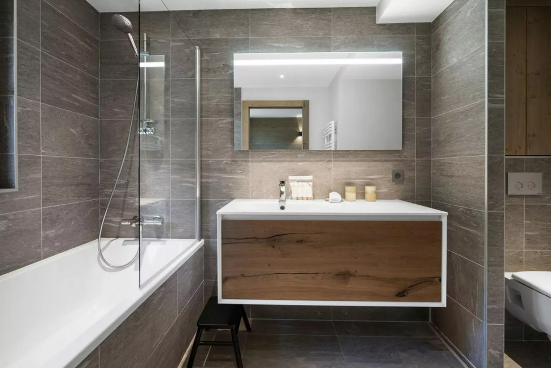 A bathroom with a bathtub and a wood-fronted vanity beneath a mirror.