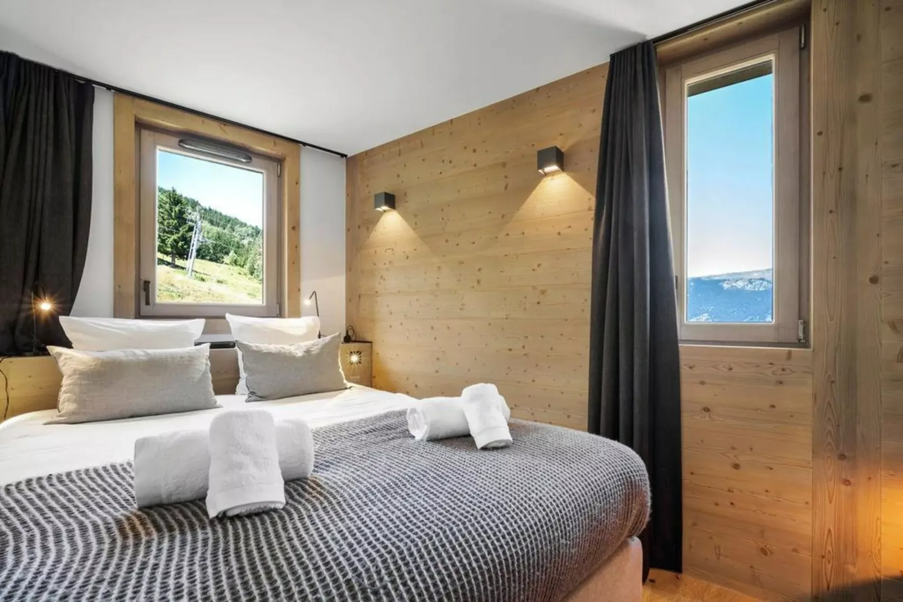 A bedroom with a bed, two windows, and dark curtains.