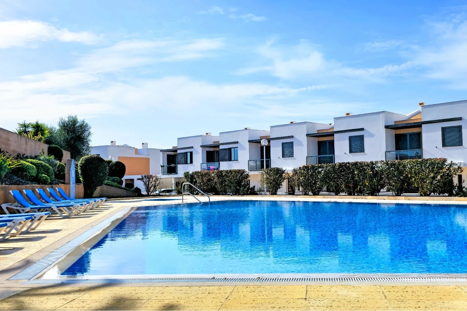 An outdoor swimming pool sits in front of a row of white buildings.