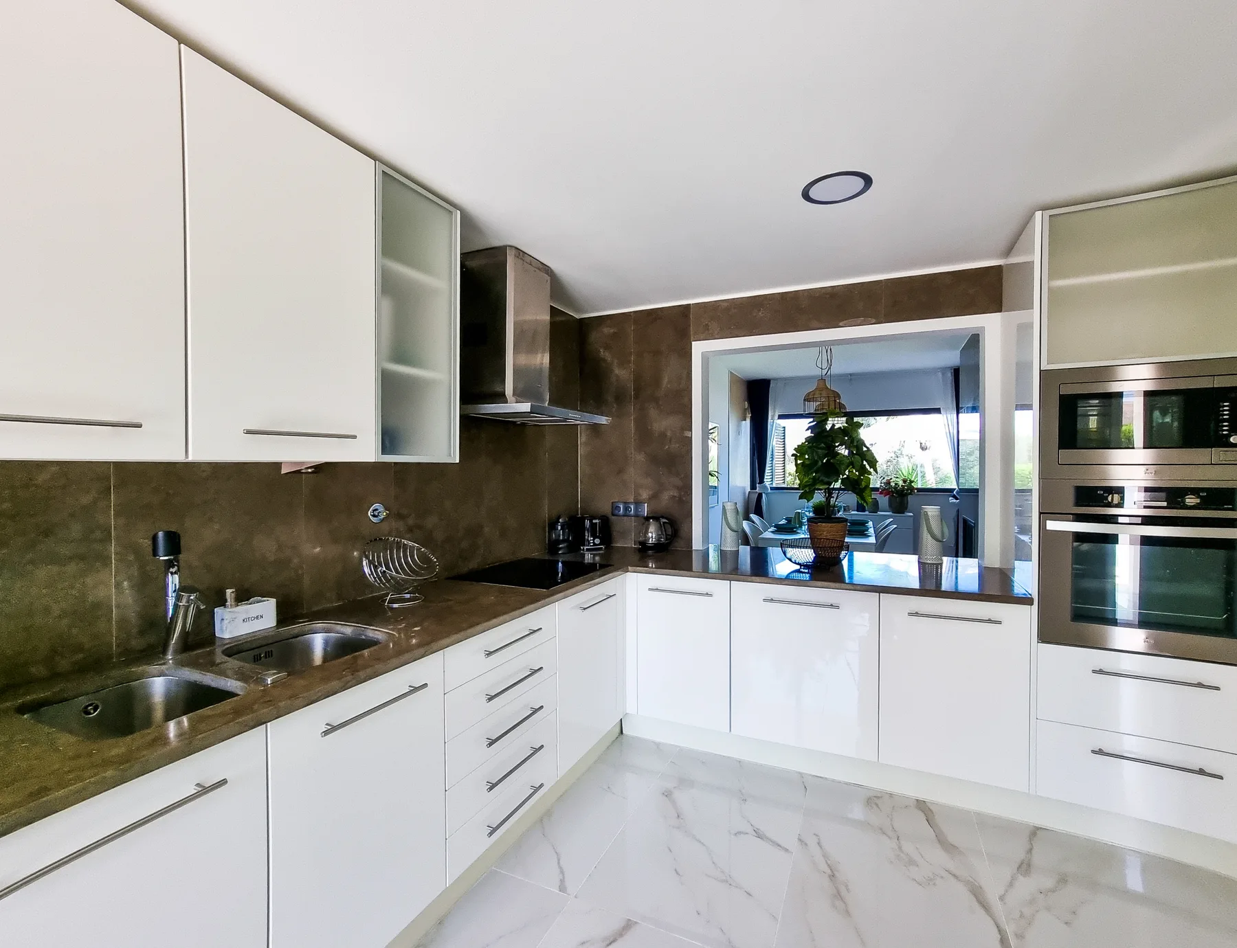 A bright kitchen with white cabinets and a counter opening onto a dining area.