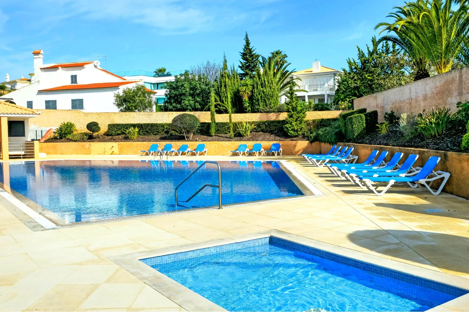 An outdoor pool area with blue loungers beside the water.