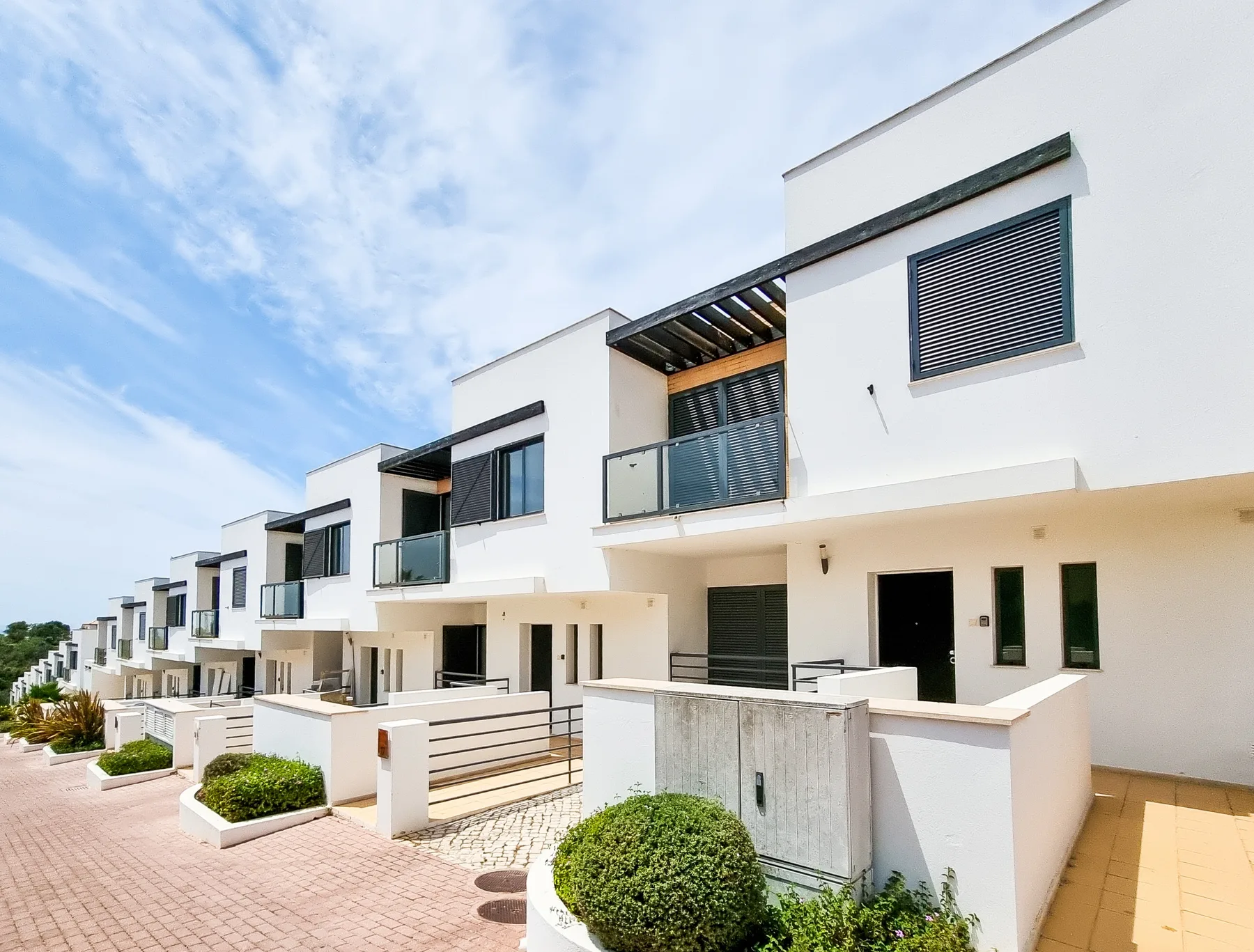 A row of modern white houses with balconies and small landscaped front areas.