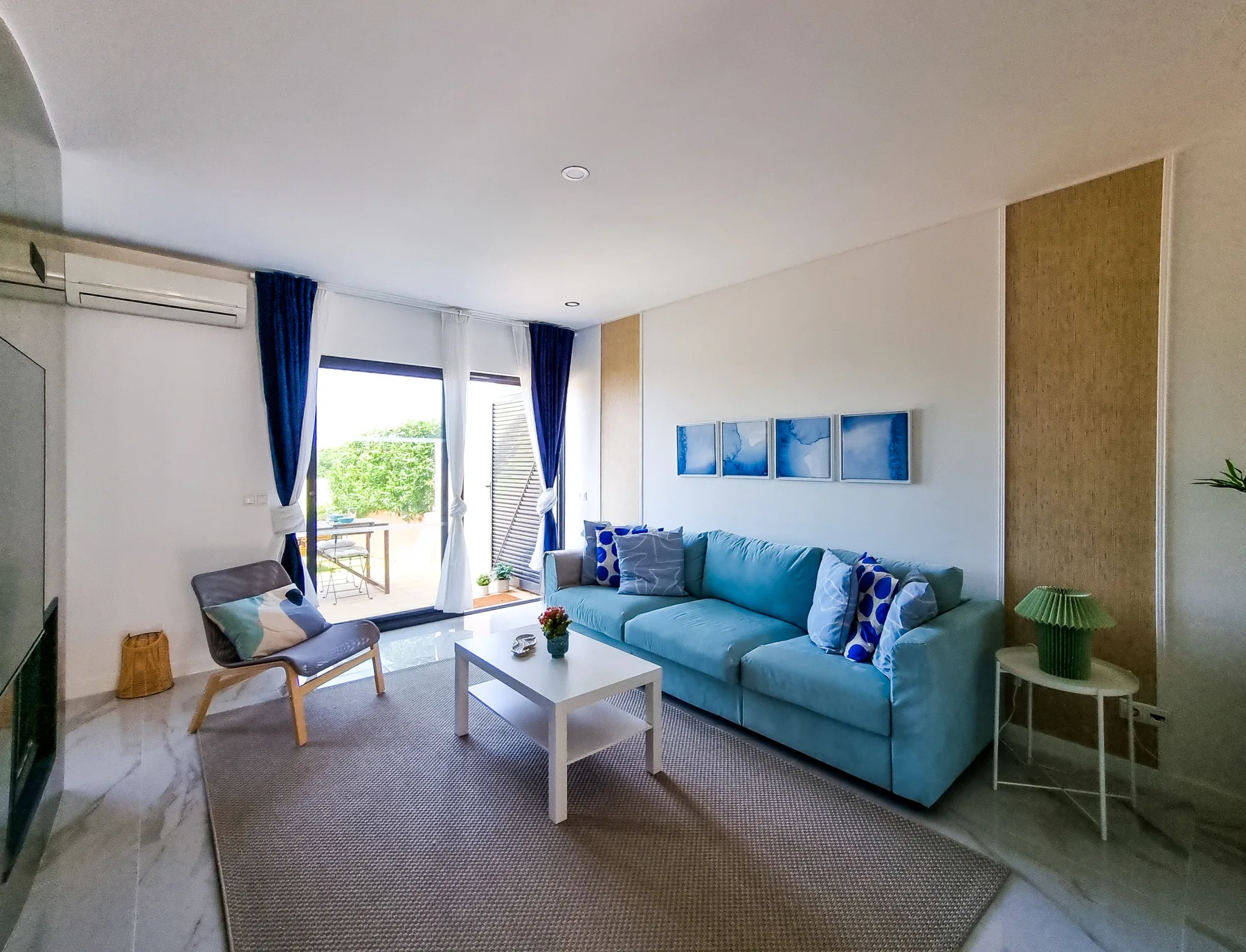 A bright living room with blue seating and glass doors opening onto a balcony.